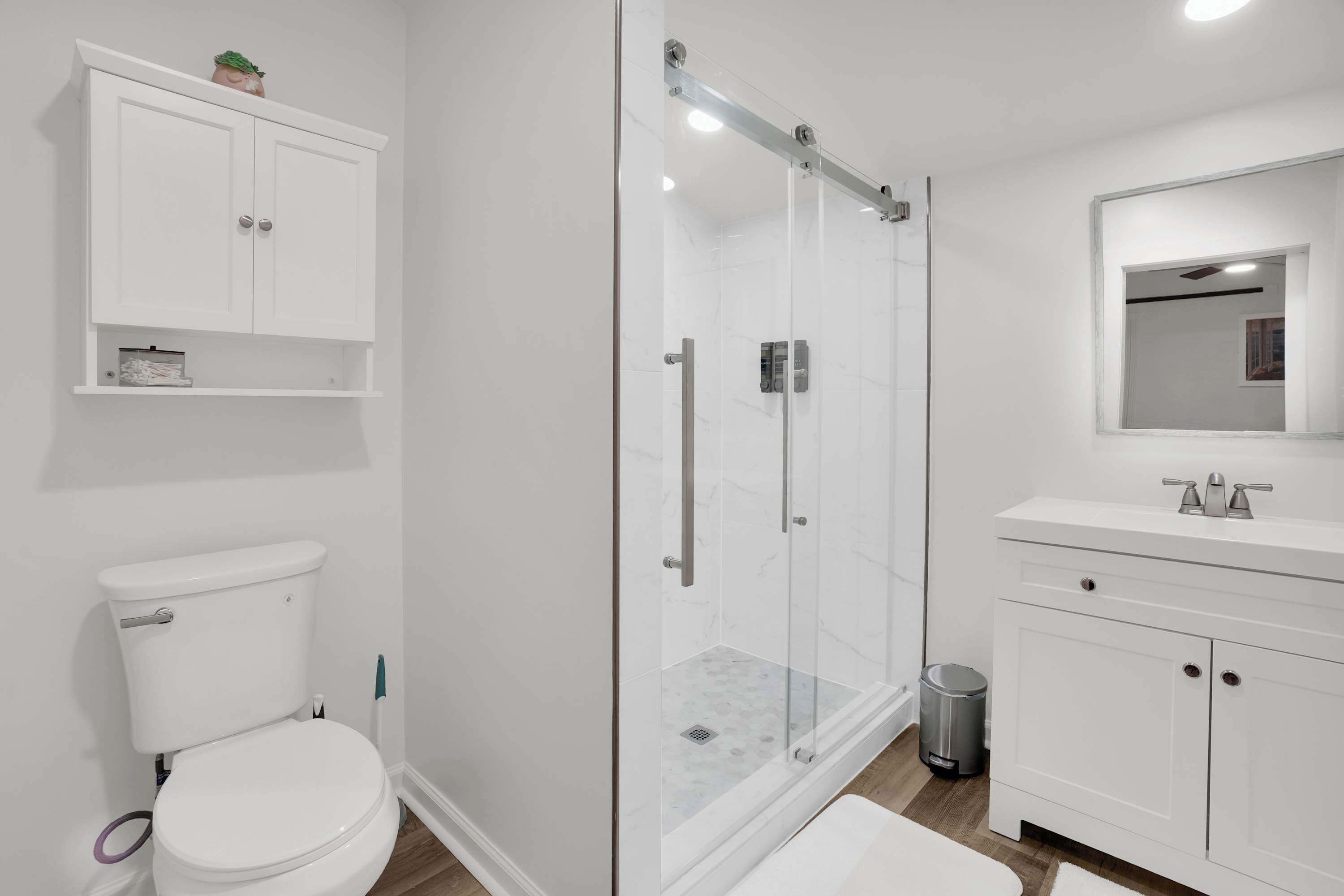 A modern bathroom with a glass-enclosed shower, white cabinetry, and a toilet.