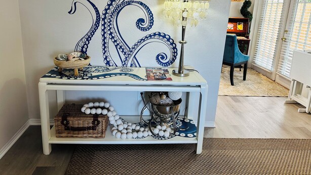 A room with a white console table featuring a blue octopus design, a yellow lamp, and a wicker basket. - Sunny St. Pete ☀️ 2 King Beds 🛌 Close to Downtown & Beaches (St. Petersburg)