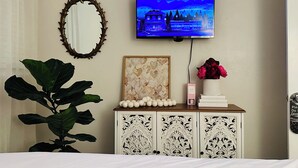 A bedroom with a TV mounted on the wall, a decorative mirror, a cabinet with a floral design, and a potted plant. - Sunny St. Pete ☀️ 2 King Beds 🛌 Close to Downtown & Beaches (St. Petersburg)