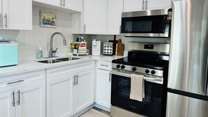A modern kitchen with white cabinets, stainless steel appliances, a microwave, a stove, and a refrigerator. - Sunny St. Pete ☀️ 2 King Beds 🛌 Close to Downtown & Beaches (St. Petersburg)