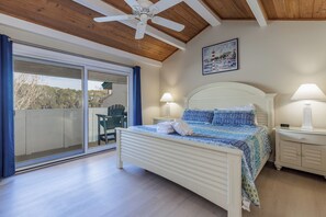 Ein Schlafzimmer mit einem Bett, zwei Nachttischen, einem Deckenventilator, einem Gemälde und einer Schiebetür zu einem Balkon.