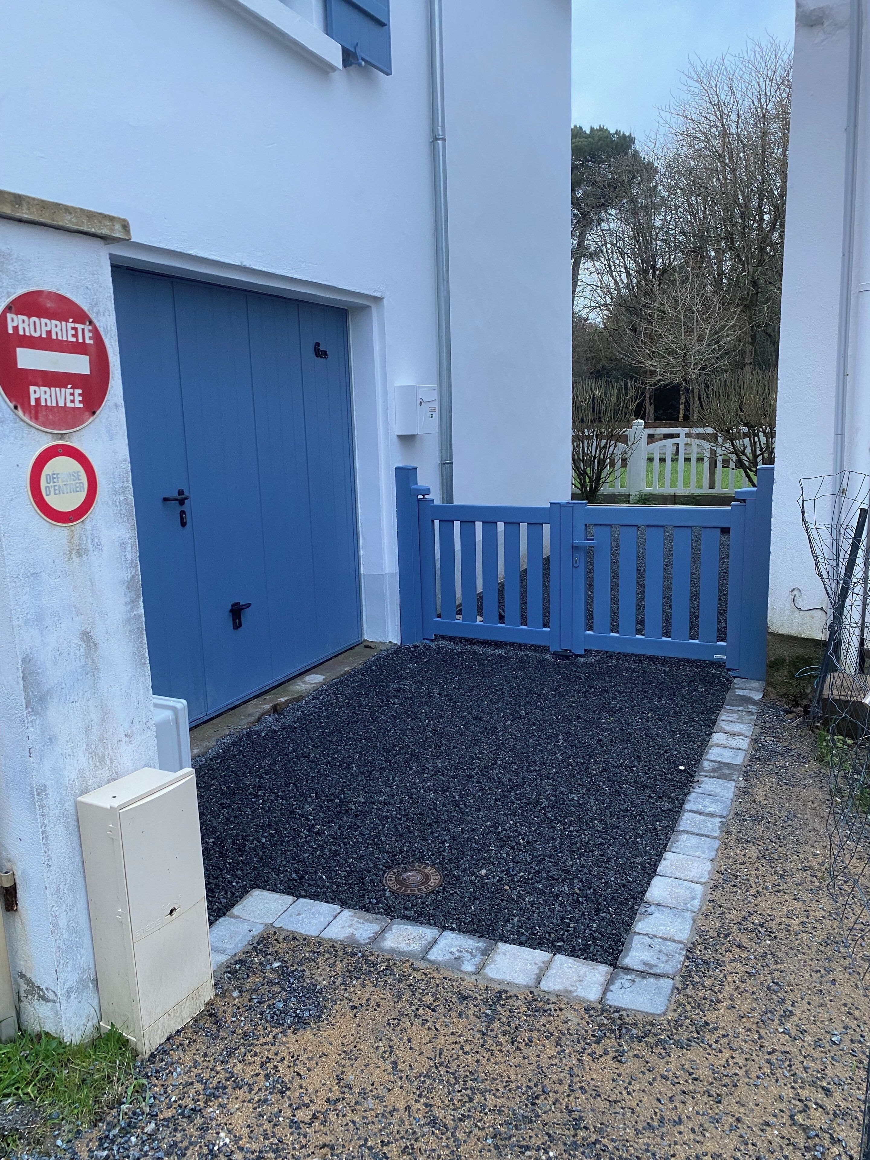 Une propriété privée avec une porte bleue, une entrée fermée par un portail et une allée gravillonnée.
