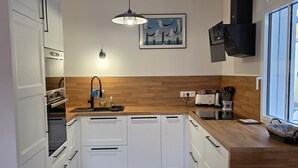 Una cocina moderna con armarios blancos, encimera de madera, suelo estampado y una lámpara colgante.