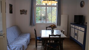 Un comedor con mesa, sillas, un florero con flores, un sofá y un aparador.