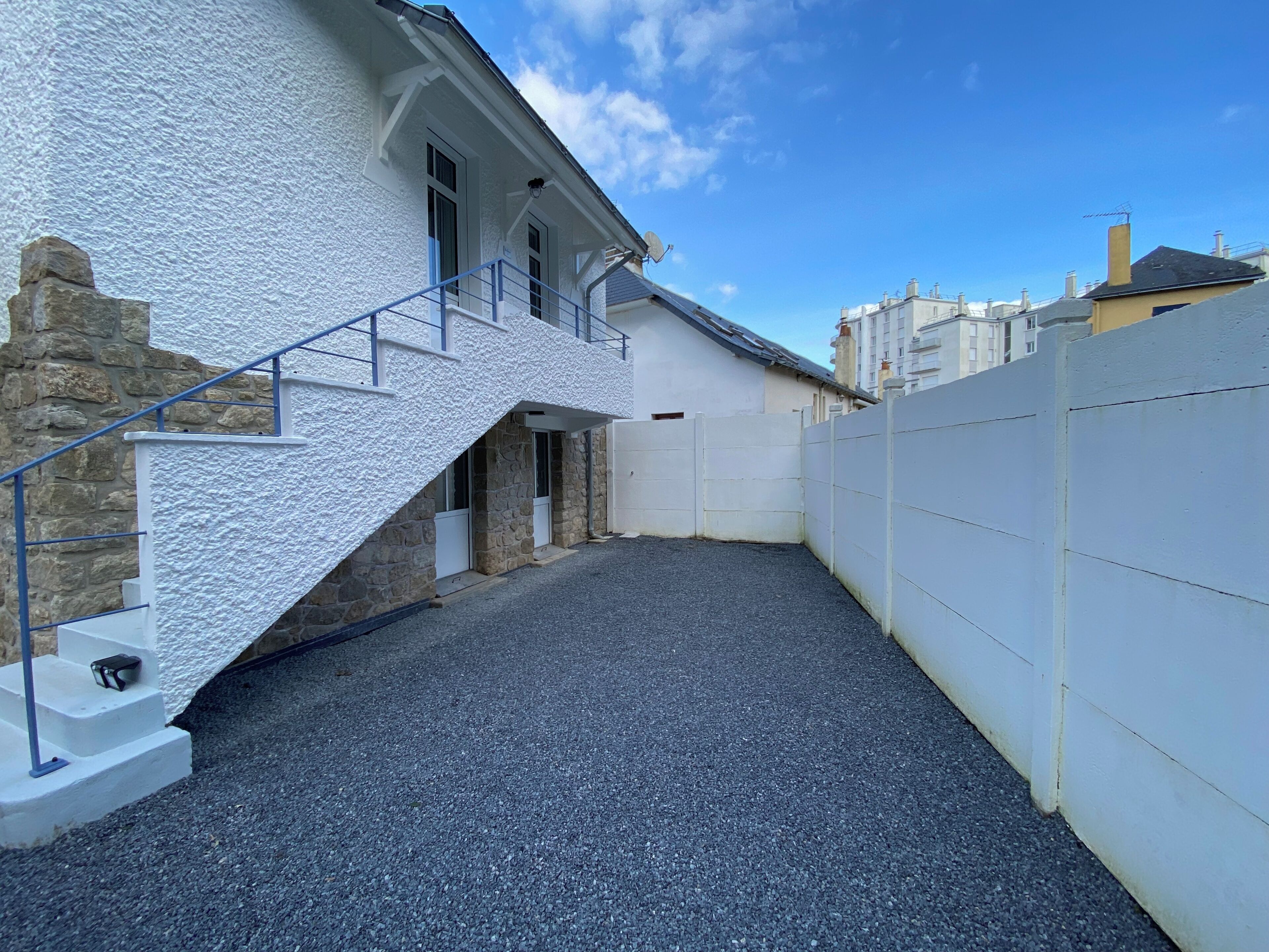 A modern building with a white exterior, a stone base, and a gravel driveway.