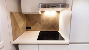 A kitchen with a built-in stove, a stainless steel range hood, and wooden wall panels. - Cosy et climatisé au coeur de Paris (Paris)