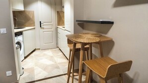 A compact kitchen with a washing machine, a small table with stools, and a built-in shelf. - Cosy et climatisé au coeur de Paris (Paris)