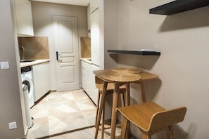 Cocina compacta con lavadora, una pequeña mesa con taburetes y un estante empotrado.
