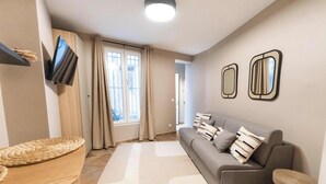 A living room with a grey sofa, two wall mirrors, a flat-screen TV, and a woven basket on a wooden table. - Cosy et climatisé au coeur de Paris (Paris)