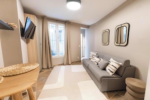 Una sala de estar con un sofá gris, dos espejos en la pared, un televisor de pantalla plana y una cesta tejida sobre una mesa de madera.