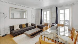 A modern living room with a glass dining table, two sofas, and a large mirror. - Appartement 2BR lumineux et raffiné - Opéra (Paris)