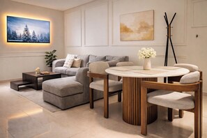 A modern living room with a sectional sofa, a round wooden table with chairs, a TV mounted on the wall, and artwork above the sofa. - Prestige Apartment Centre Agdal Rabat (Rabat)