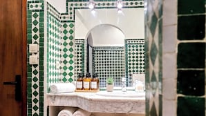 A bathroom with a green and white checkered tile backsplash, a marble countertop, and a mirror above it. There are towels, a small plant, and toiletries on the counter. - Prestige Apartment Centre Agdal Rabat (Rabat)