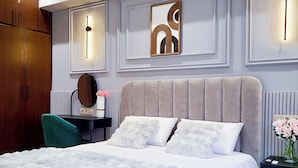 A bedroom with a bed, a nightstand, a dresser, a mirror, and wall-mounted lighting. - Prestige Apartment Centre Agdal Rabat (Rabat)