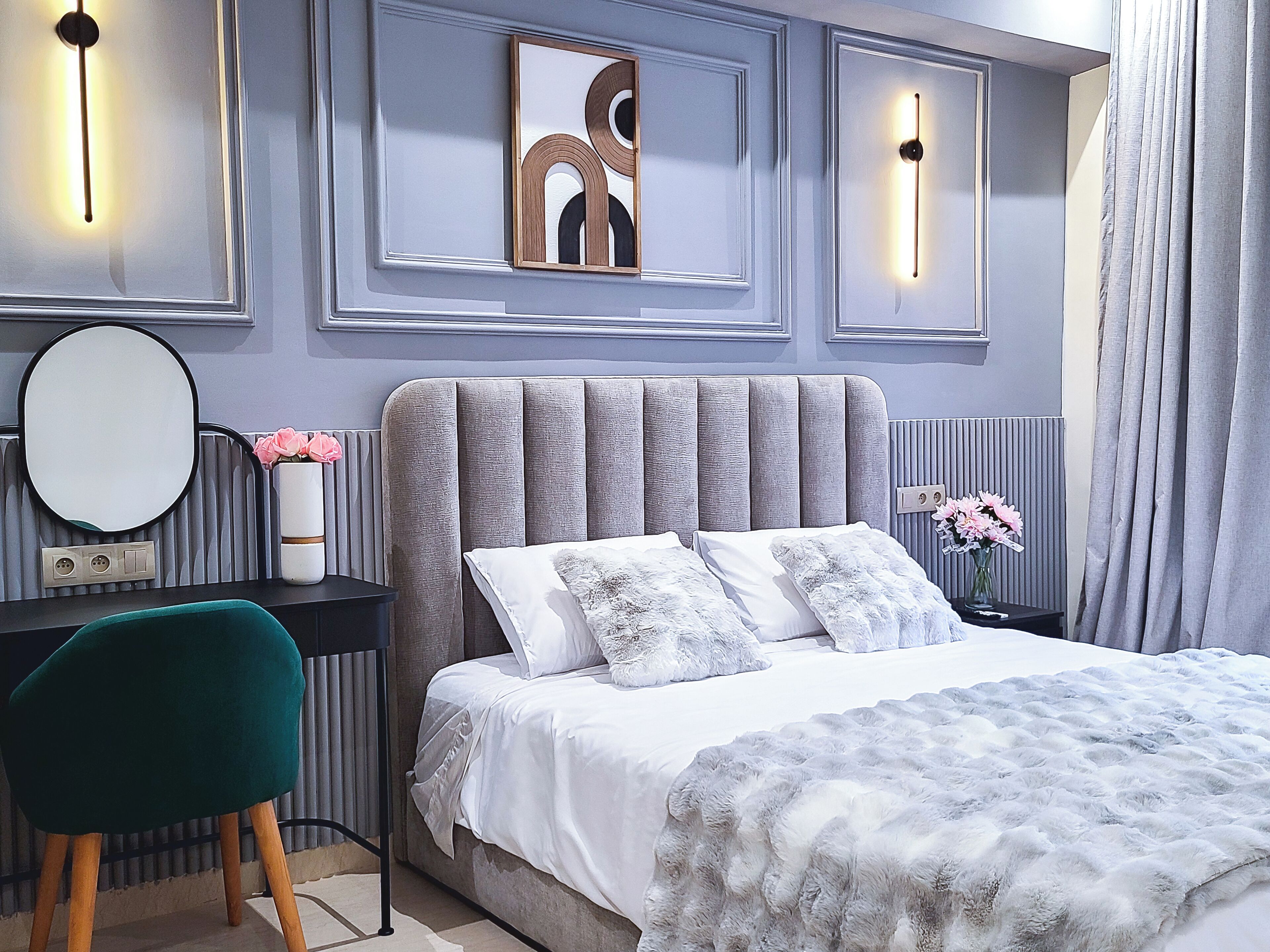 Un dormitorio con una cama grande, una mesita de noche y una silla. Hay luces fijadas a la pared y un radiador.