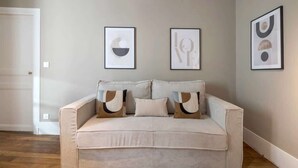 A living room with a beige sofa, two framed abstract art pieces, and a white door. - Modern apartment with AC in the heart of the 7th arrondissement (Paris)