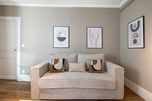 A living room with a beige sofa, two framed abstract art pieces, and a white door. - Modern apartment in the heart of the 7th arrondissement (Paris)