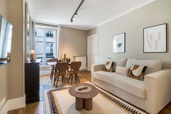 A modern living room with a sofa, a coffee table, and a dining area with chairs and a table. - Modern apartment in the heart of the 7th arrondissement (Paris)