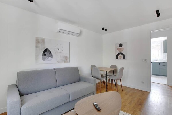 A modern living room with a grey sofa, a round coffee table, and a dining area with a small table and chairs.