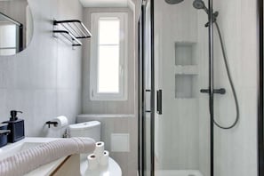 A modern bathroom with a glass shower enclosure, a toilet, and a sink with a towel.