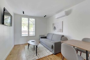 A modern living room with a grey sofa, a small white table, and a wooden dining table with chairs.