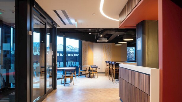 A modern interior with a bar area, seating, and large windows. - Student Only Haymarket Yard (Edinburgh)