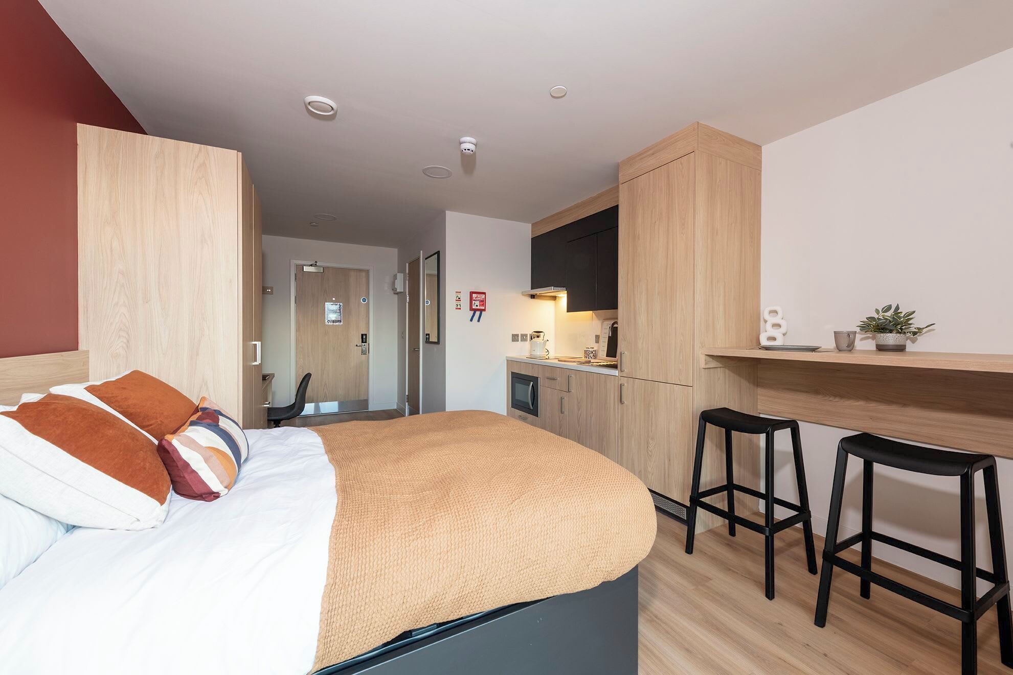 Ein modernes Hotelzimmer mit Bett, einer Küchenzeile, einer kleinen Essecke und einem Badezimmer.