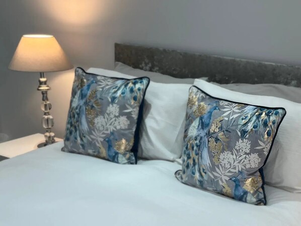 Ein Bett mit zwei dekorativen Kissen mit blauem und goldenem Blumenmuster, einer Nachttischlampe und einem grauen Kopfteil.