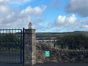 A stone wall with a metal gate, a stone lion statue, and a green sign indicating a fire assembly point. - Belstane Manor B&B (Carluke)
