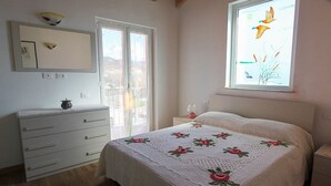 Et soveværelse med seng, kommode, sengebord, et vindue med udsigt til fugle og en vægmonteret lampe.