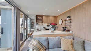 Un salon moderne avec un canapé gris, une table basse et un coin cuisine doté de meubles en bois et d’un four encastré.