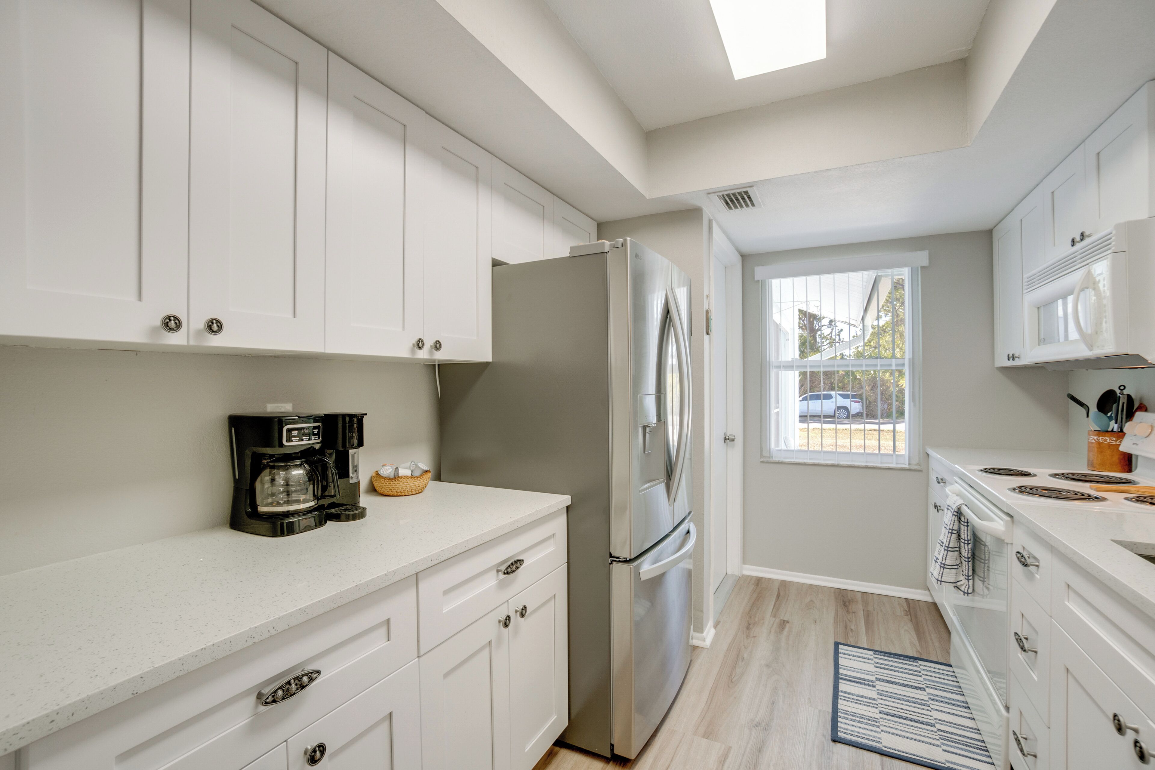 Une cuisine moderne avec des meubles blancs, un réfrigérateur en acier inoxydable, une machine à café et une fenêtre donnant sur l’extérieur.