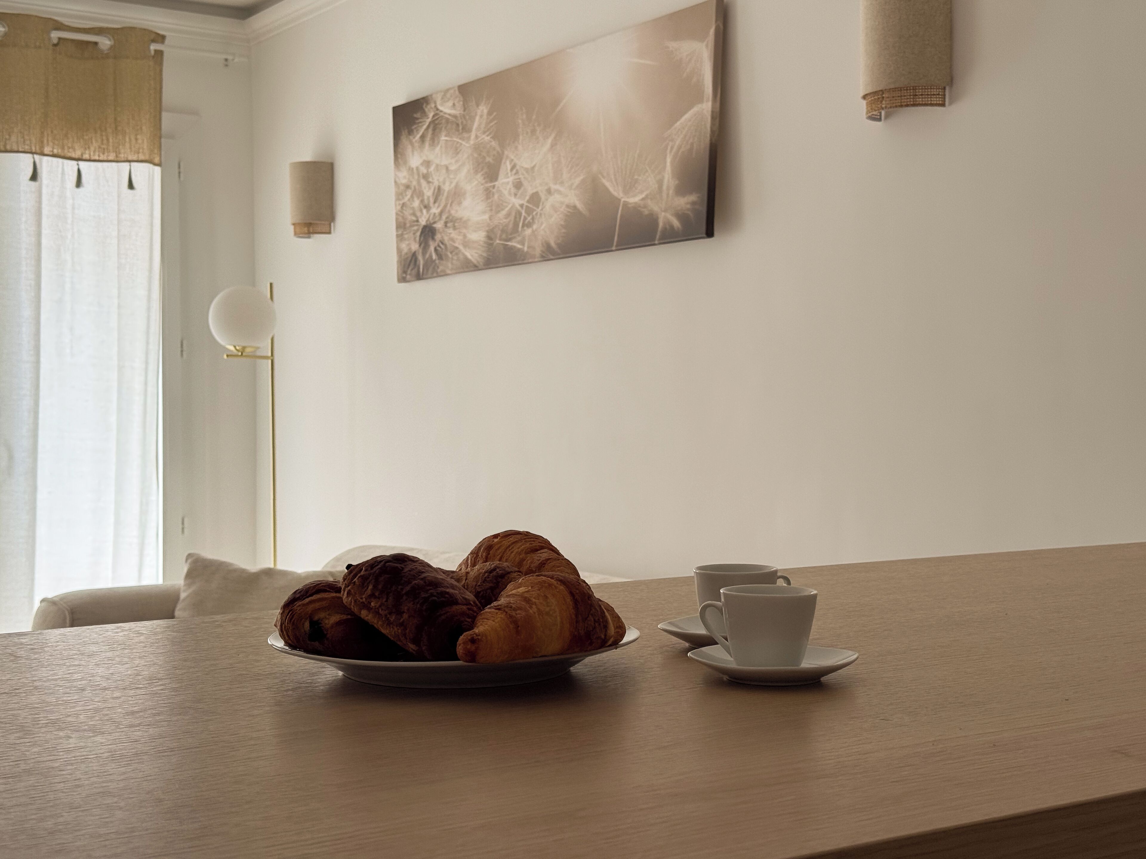 Una mesa de comedor con un plato de croissants y una taza y platillo.