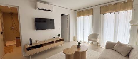 A modern living room with a flat-screen TV, a sofa, two round coffee tables, a sideboard, and a shower area.