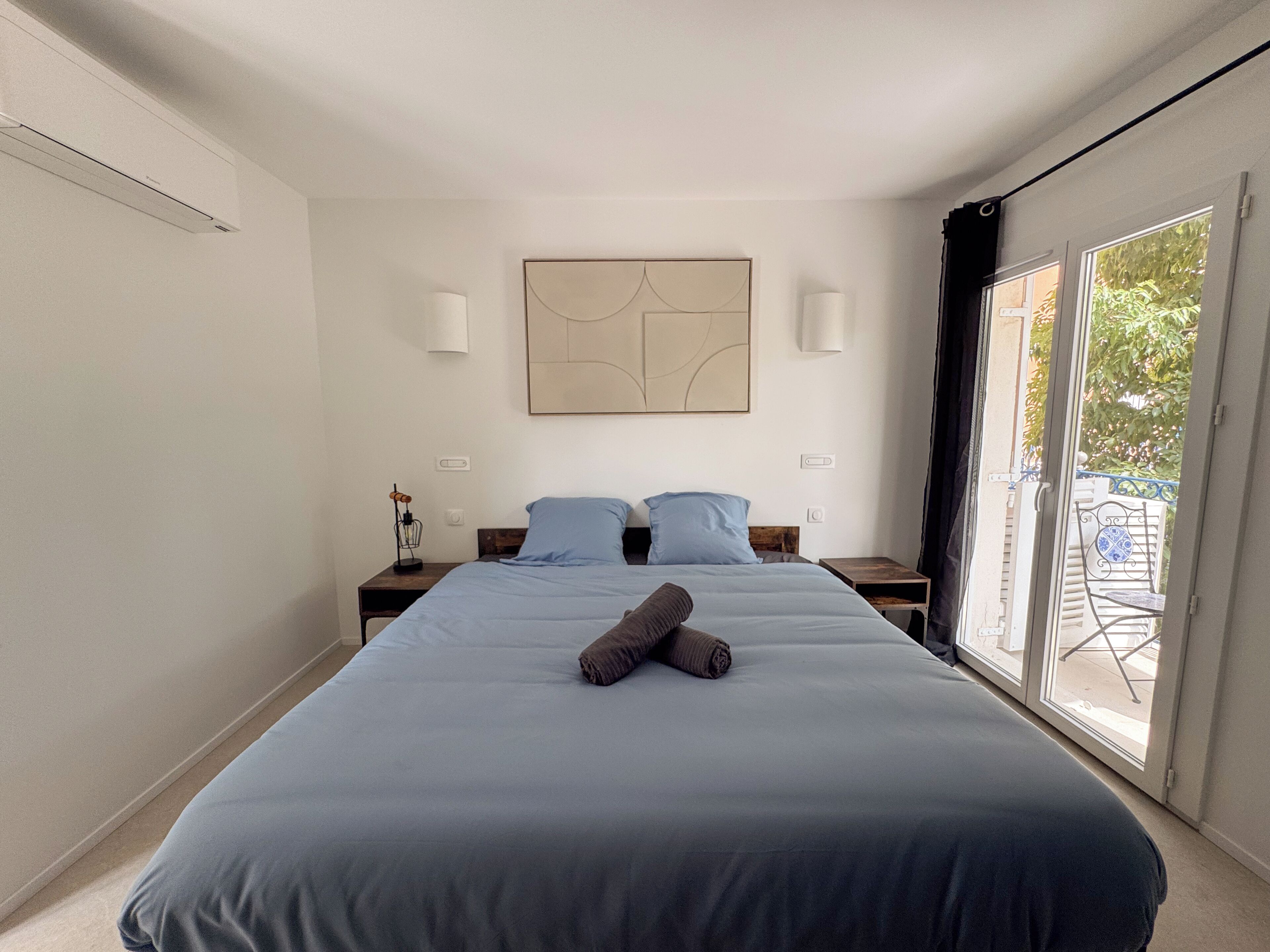 A bedroom with a large bed, two bedside tables, a wall-mounted artwork, and a sliding glass door to the outside.