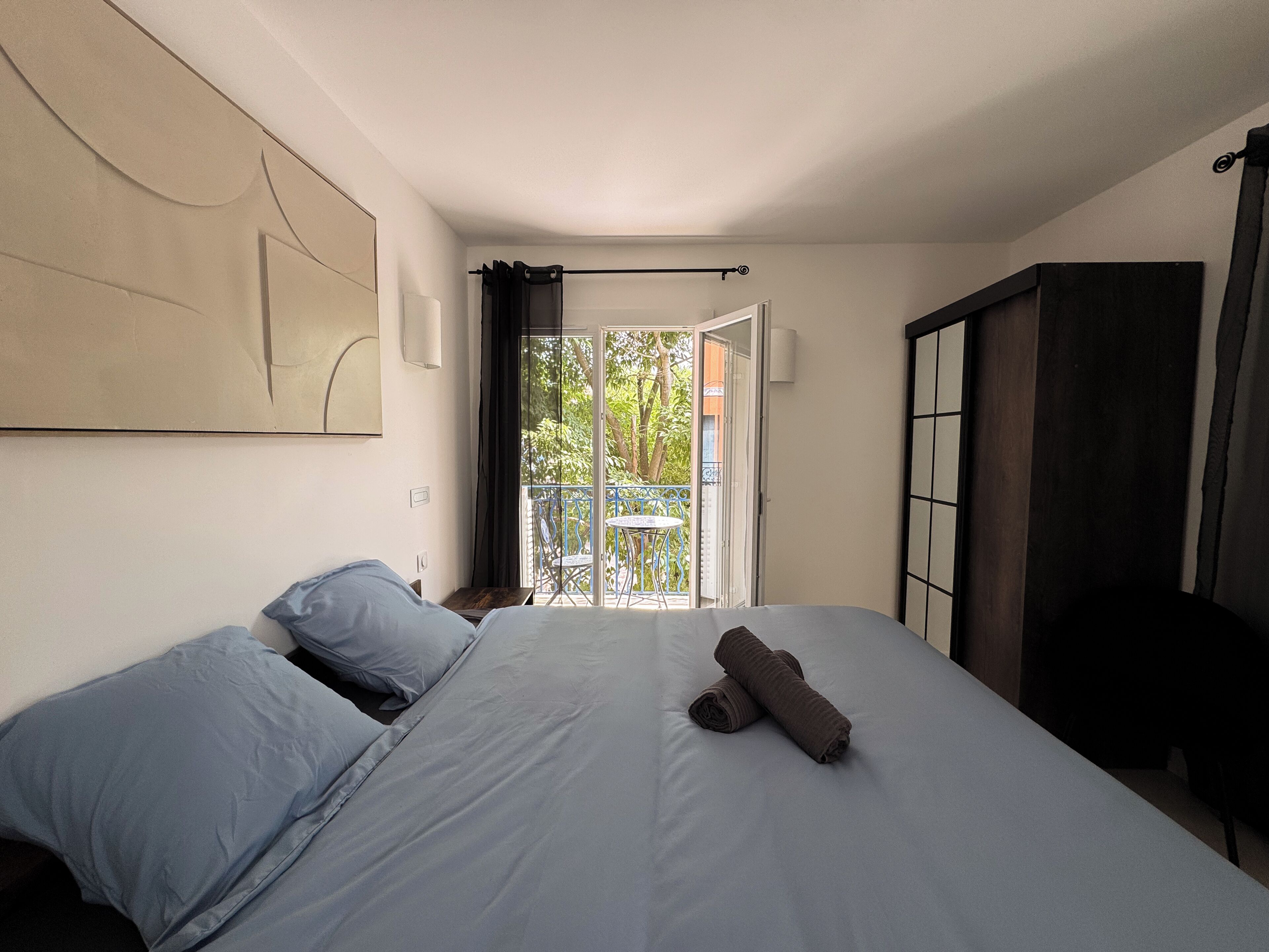 Un dormitorio con cama, armario, balcón con mesa y sillas, y puerta de acceso al exterior.