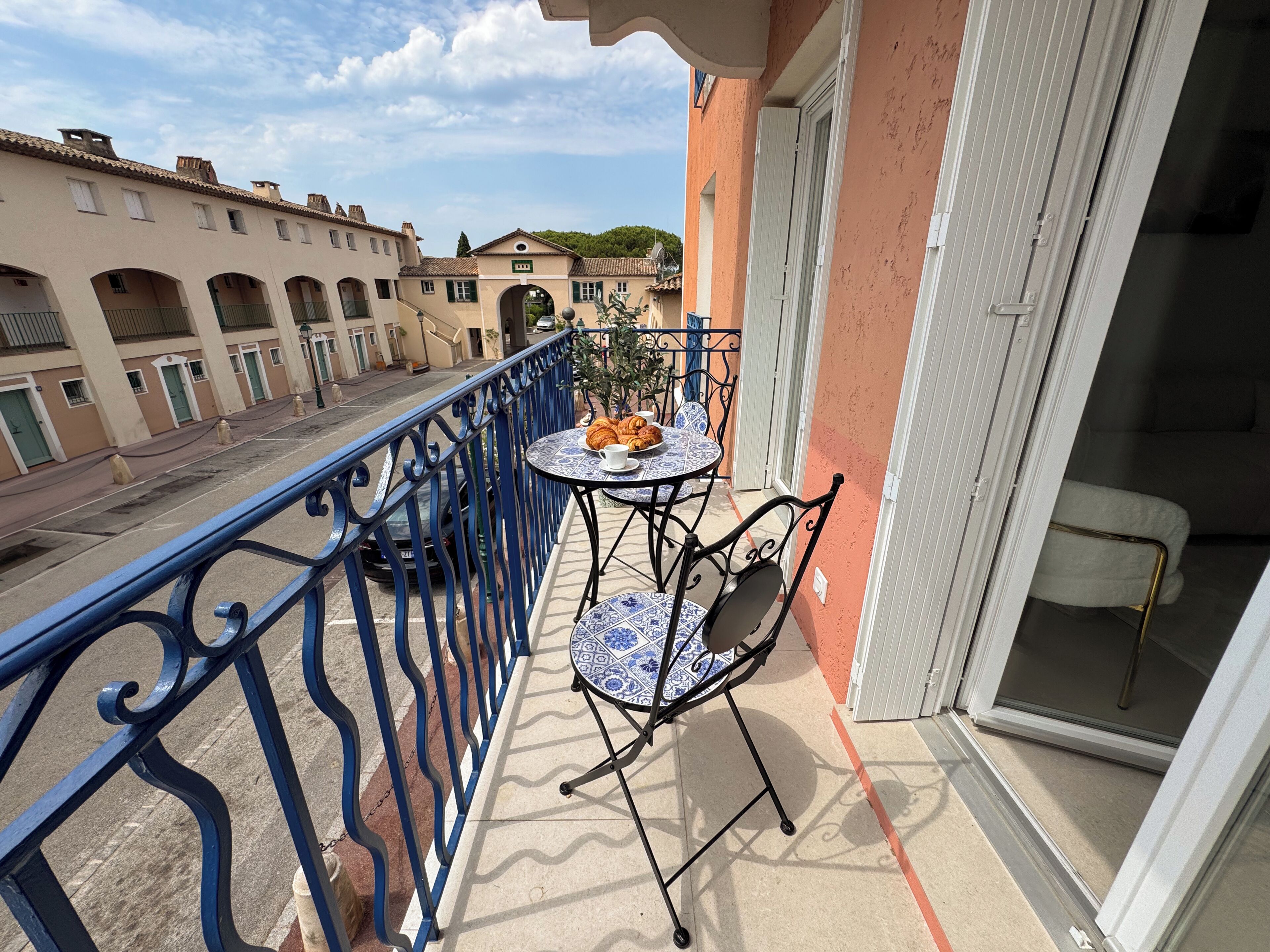 A balcony with a table and chairs, a view of the street, and a building with a tiled roof.