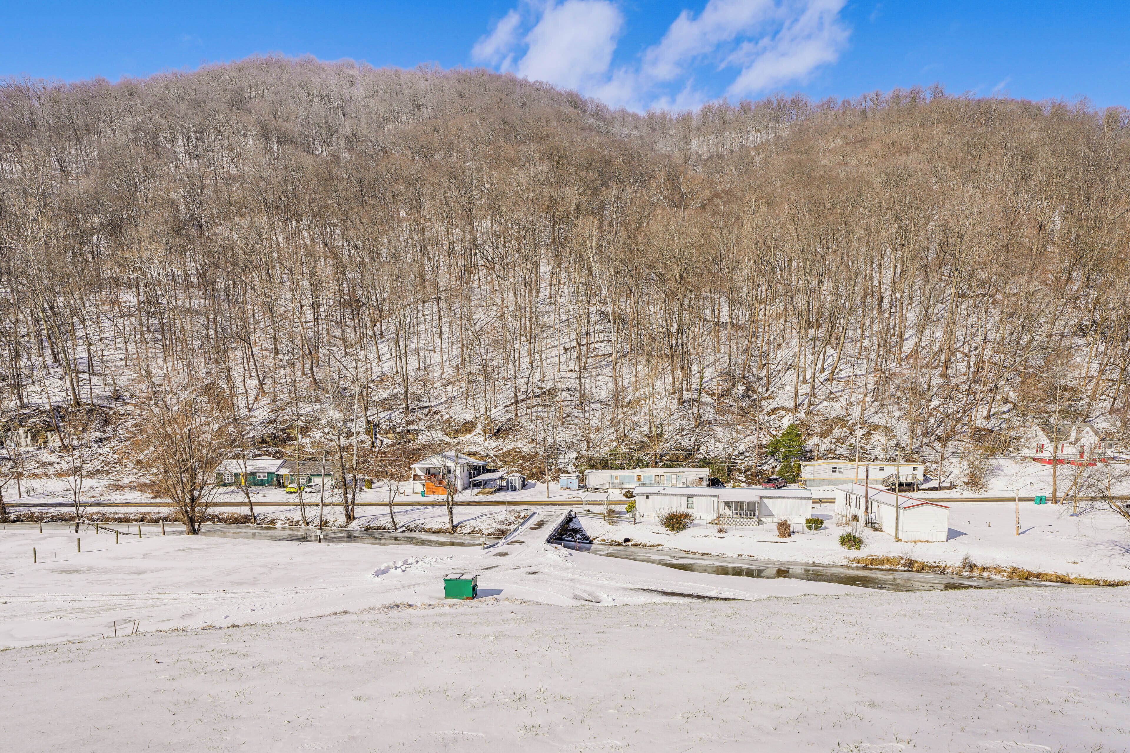 A snowy landscape with a river, buildings, and a forested hill.