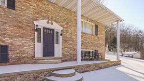 A brick house with a white porch, a black door, and a small outdoor seating area. - Pool Table + Private Porch: Peaceful Apt in Belle (Belle)