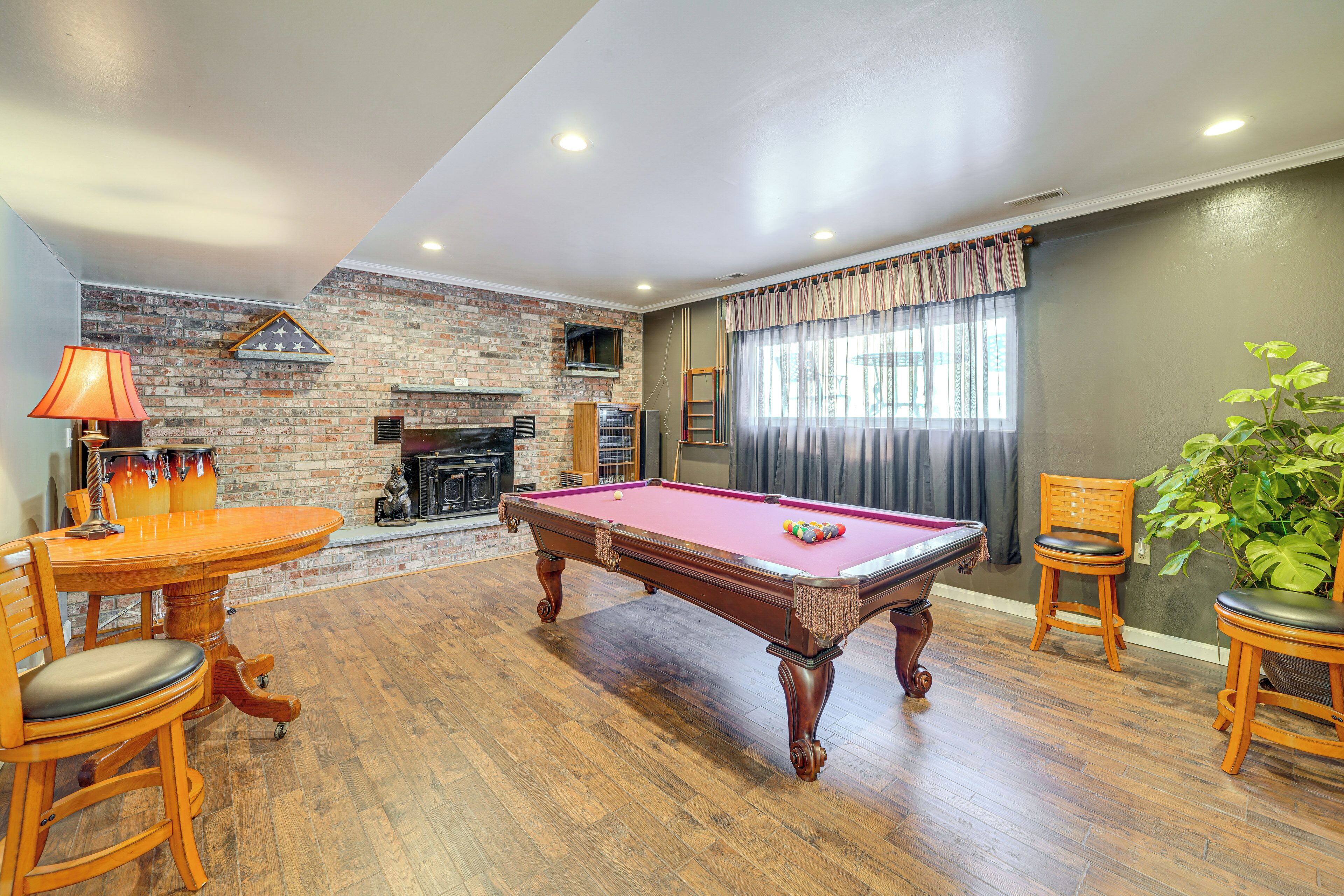 A pool table in a room with wooden flooring, a brick wall, and a fireplace.
