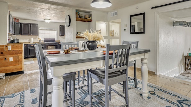 A modern kitchen with dark cabinets, a central island, and a dining area with a table and chairs.
