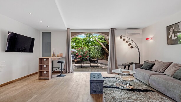 A modern living room with a sofa, a coffee table, a TV mounted on the wall, and a dining area with a table and chairs. - Happy Tropez: Authentic village house with terrace, in the heart of Gassin. (Gassin)