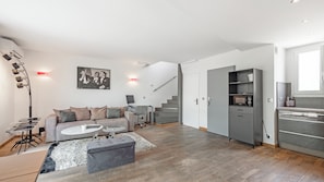 Un espacio habitable moderno con sofá, mesa de centro, reposapiés y una zona de cocina con microondas y armarios.