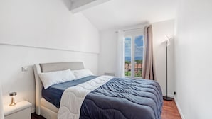 A bedroom with a bed, a bedside table, a floor lamp, and a window with a view. - Happy Tropez: Authentic village house with terrace, in the heart of Gassin. (Gassin)
