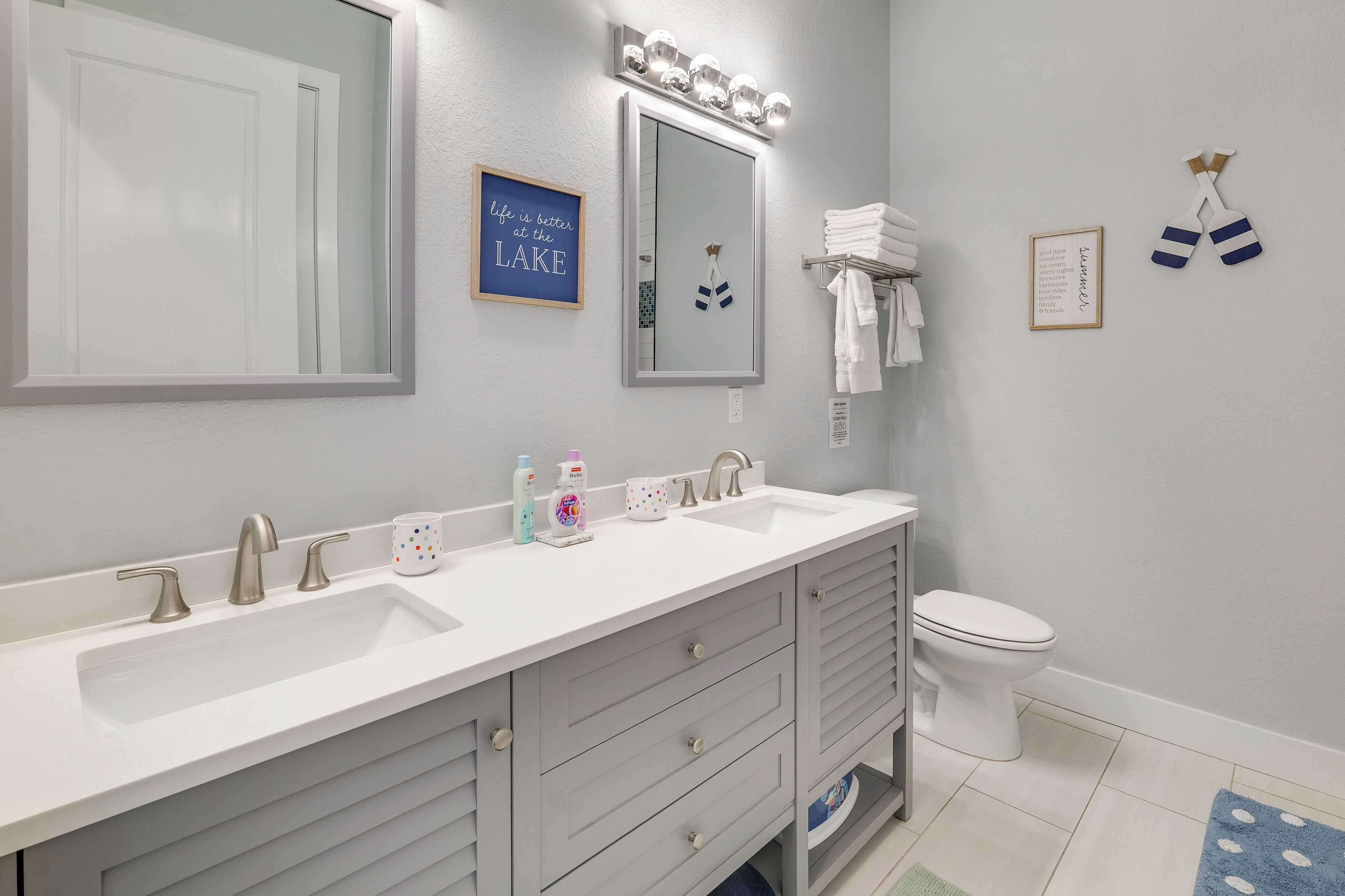 A bathroom with a white vanity, two sinks, a mirror, and a toilet.