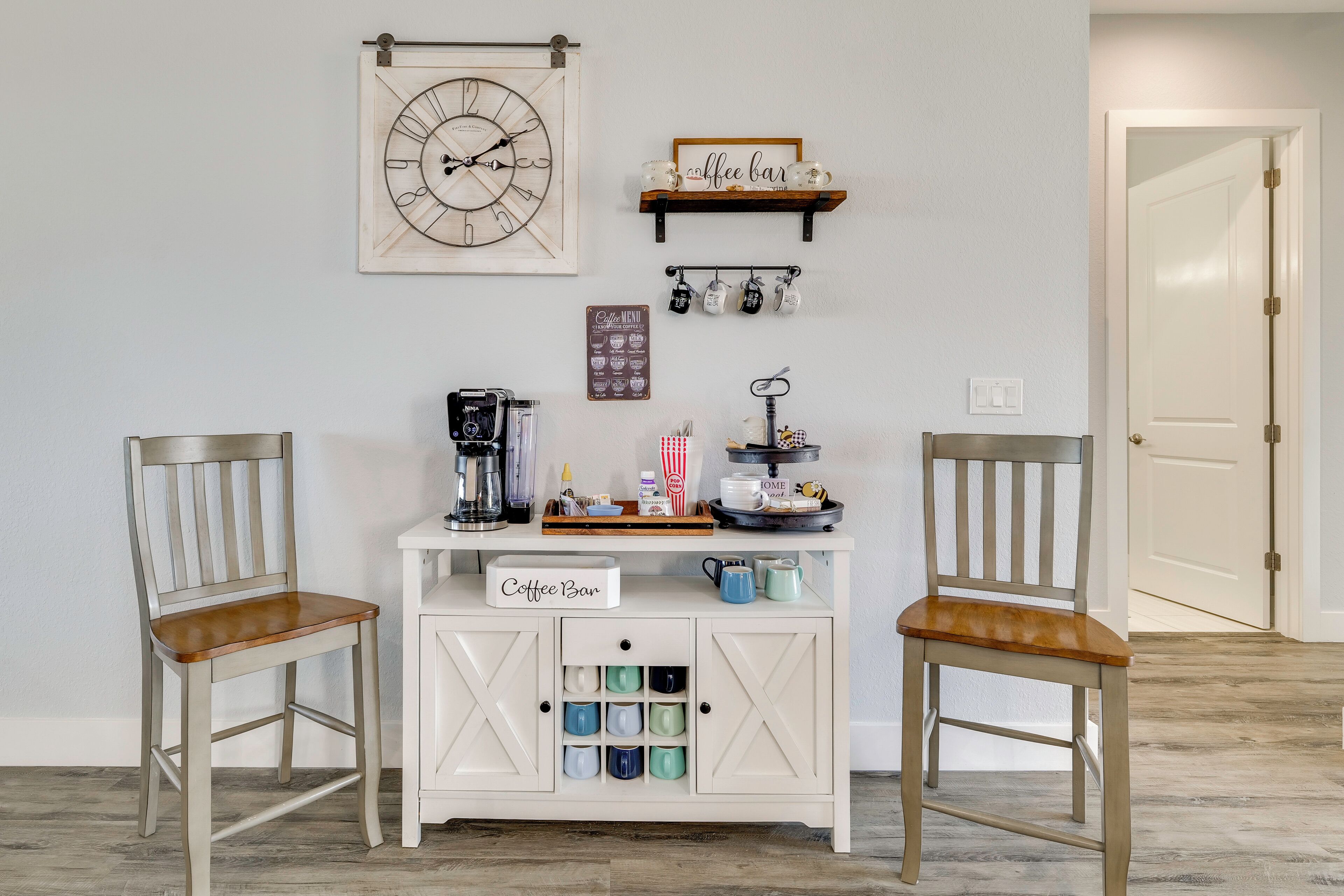 A coffee bar setup with two chairs, a clock, and a coffee menu on the wall.