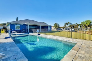 A swimming pool area with a blue building, a fenced patio, and a clear sky.