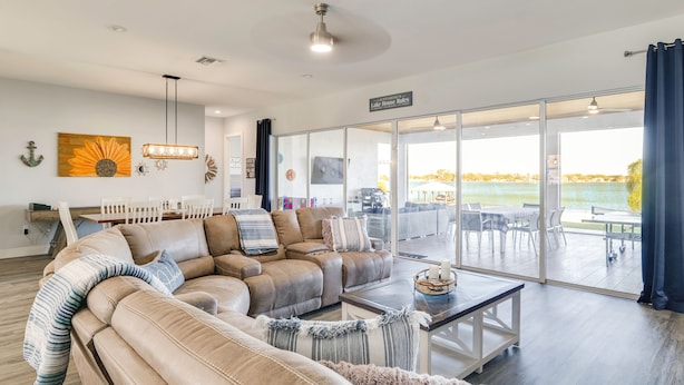 A spacious living room with a large sectional sofa, a dining area, and a view of a lake through large sliding glass doors. - Poolside Paradise & Boat Dock! Haven on Lake Clay (Lake Placid)