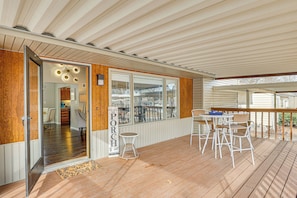 Eine überdachte Holzterrasse mit weißen Geländern und einer Sitzgruppe mit weißen Stühlen und einem Tisch.