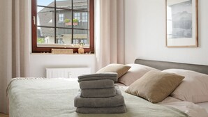 Un dormitorio con cama, almohadas, una ventana y un cuadro en la pared.